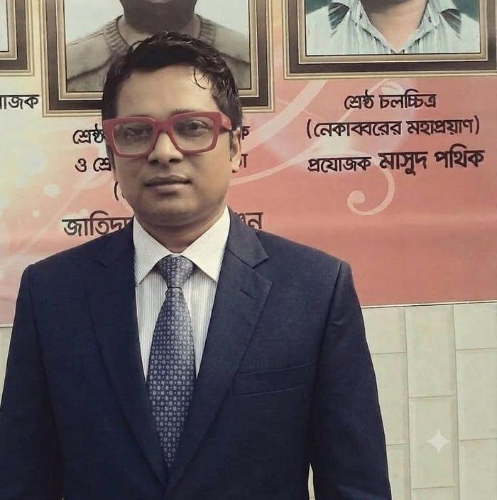 Masud Pathik in a suit in front of the National Film Award banner for Nekabborer Mohaproyan