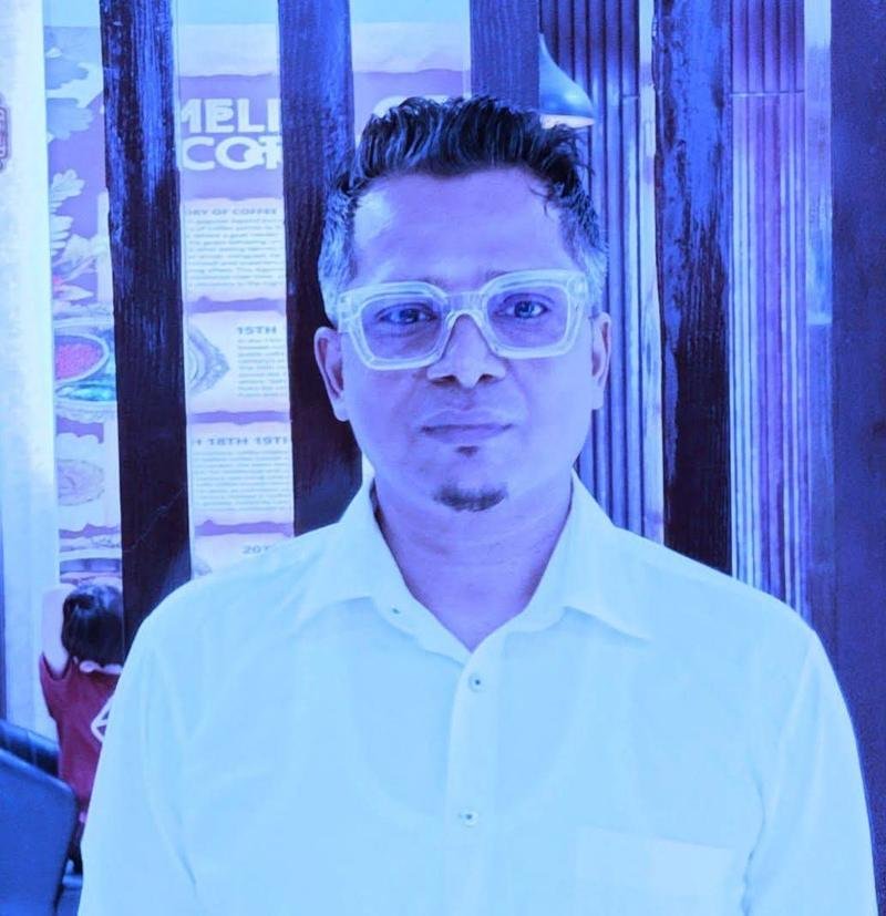 Portrait of Masud Pathik in a white shirt and clear glasses