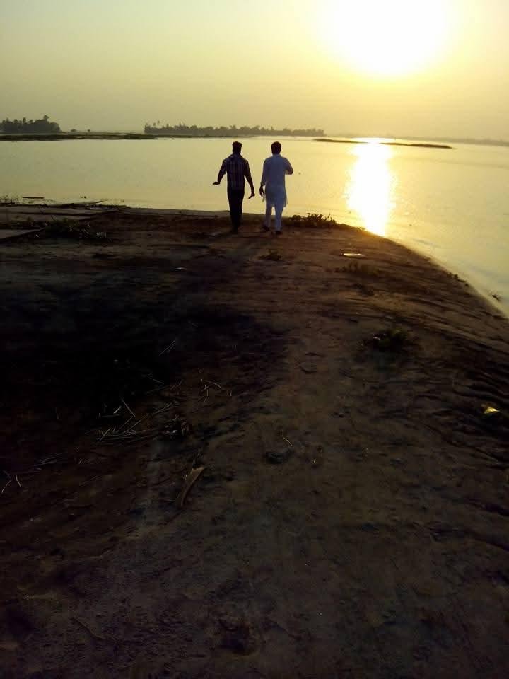 Two men walking toward a river at sunset along a sandy bank